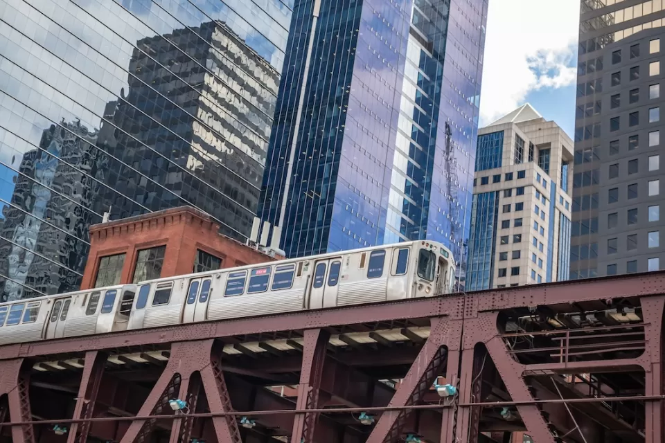 View up at Chicago elevated train line with train passing and glass high-rises in background.